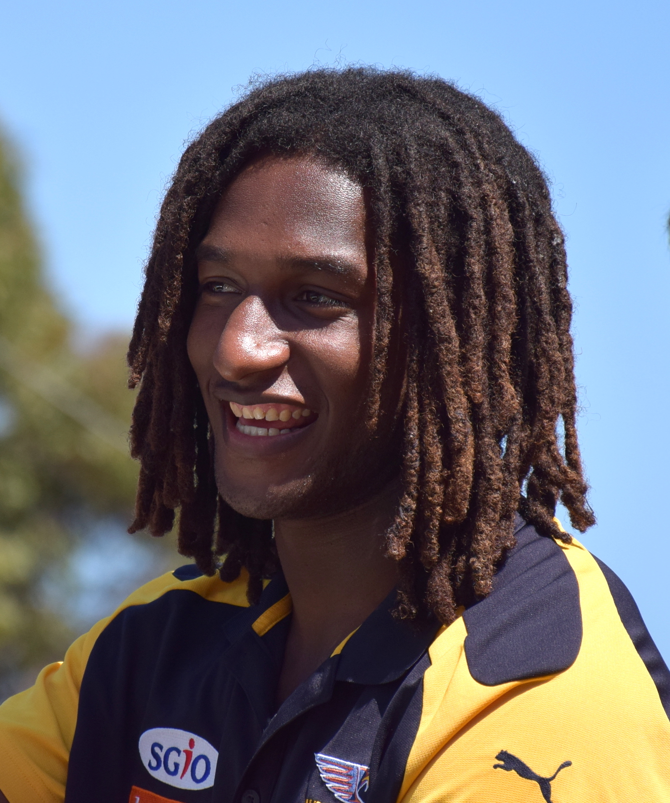 A smiling athlete in a yellow and black sports uniform celebrates the AFL Grand Final, showcasing Melbourne's vibrant.