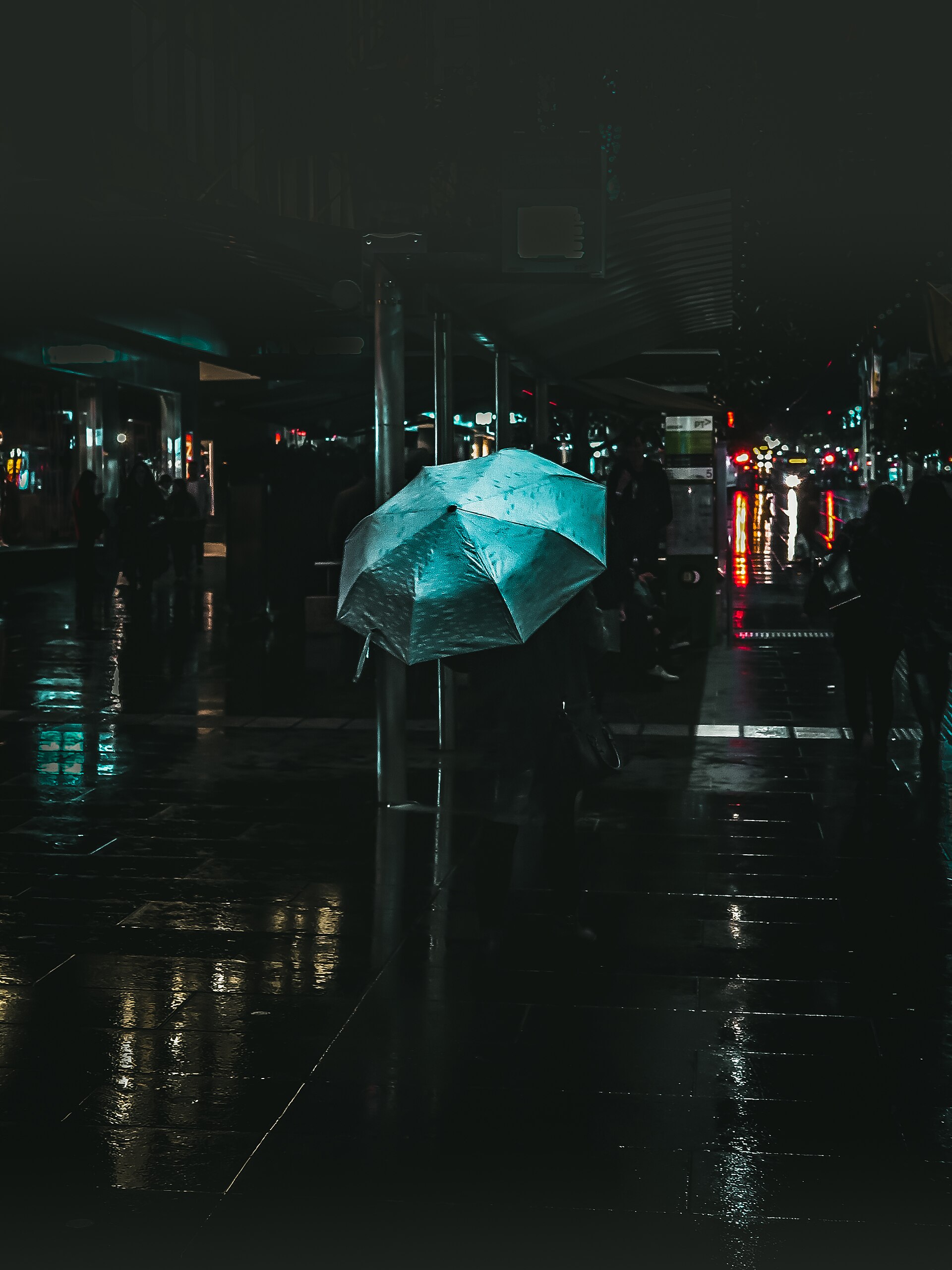 A rainy city street scene with a teal umbrella shows Melbourne lifestyle and culture.