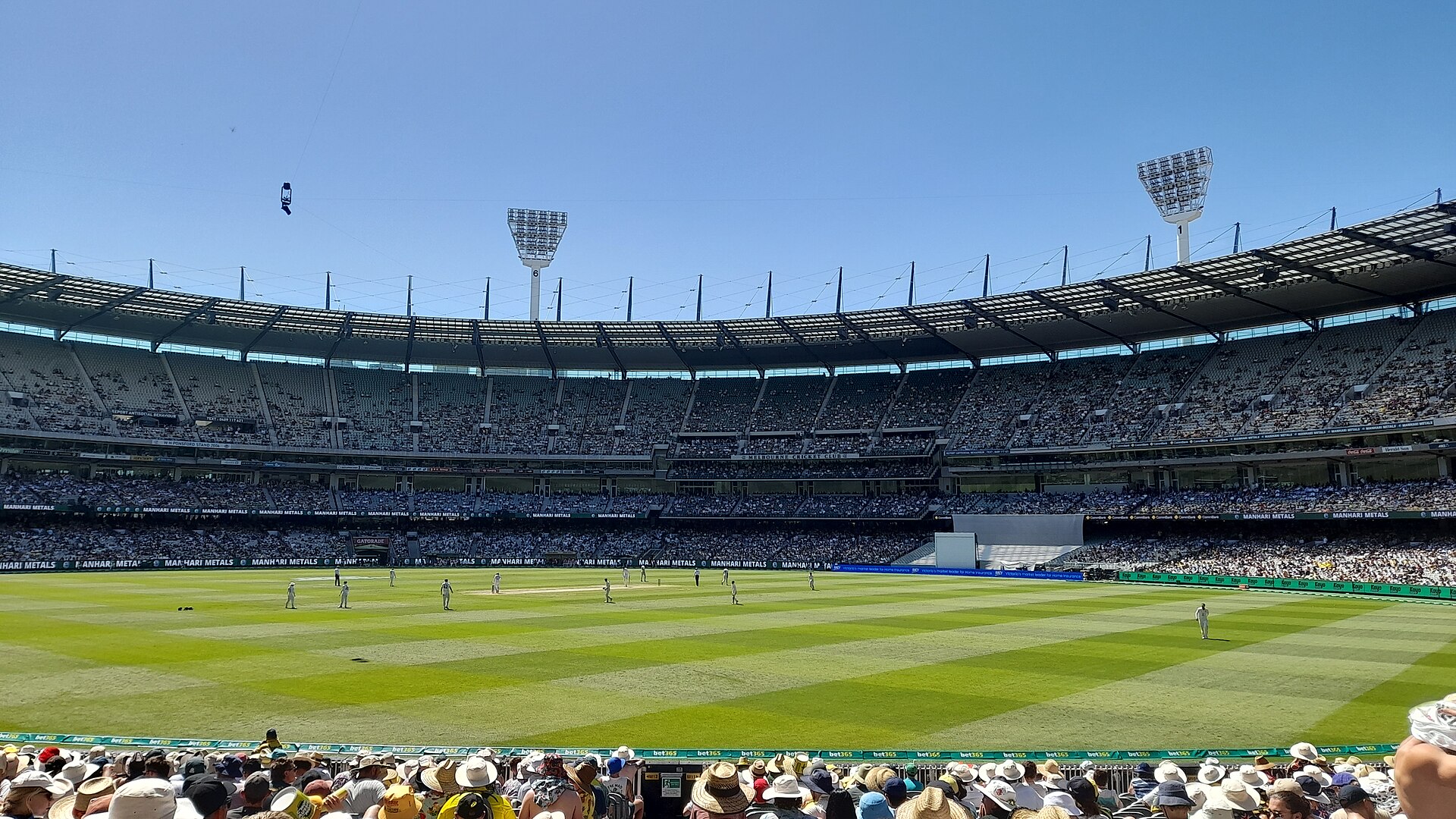 A sunny day at the Melbourne Cricket Ground with a packed crowd enjoying a cricket match.