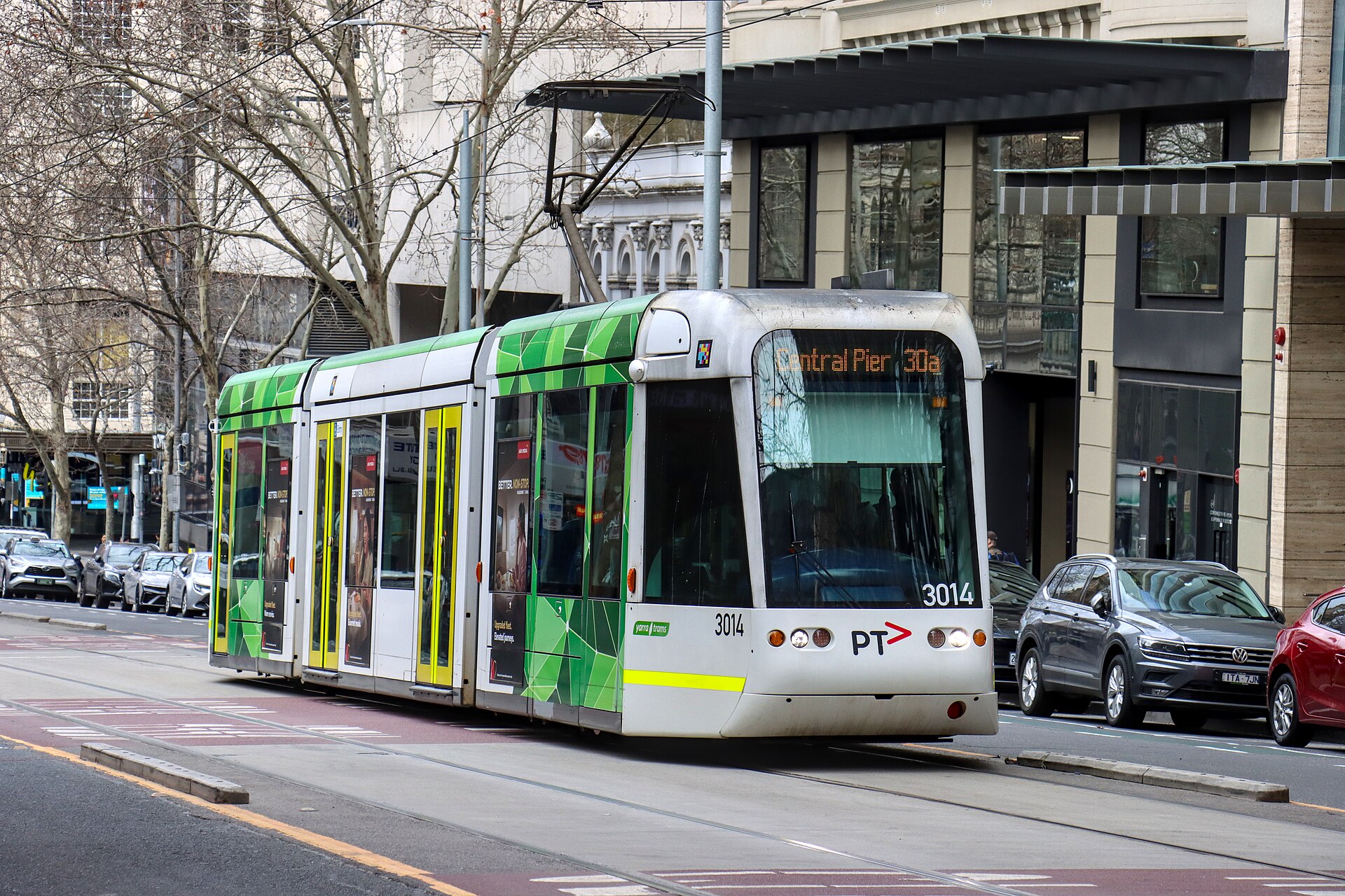 A green tram travels down a city street in Melbourne, showcasing local transport options.