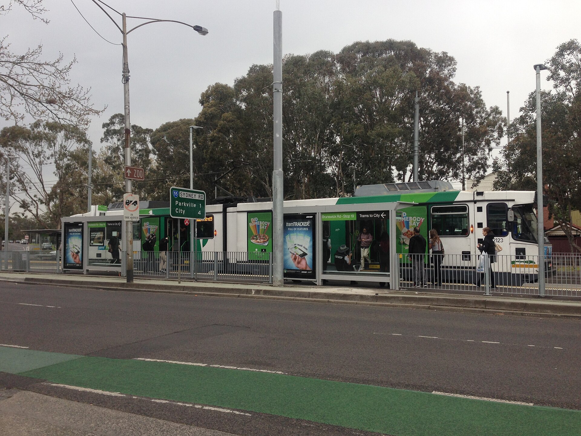 A green and white tram stops at a station, showcasing advertising as part of Melbourne's public transport system.