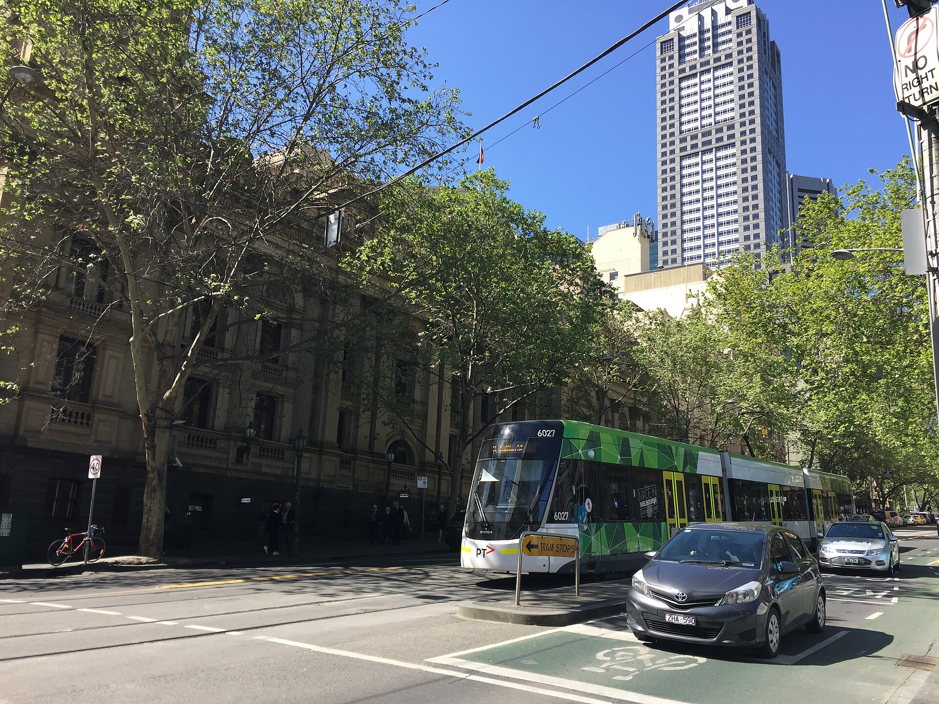 A green tram travels along a Melbourne street, showcasing local life and the city's transport.