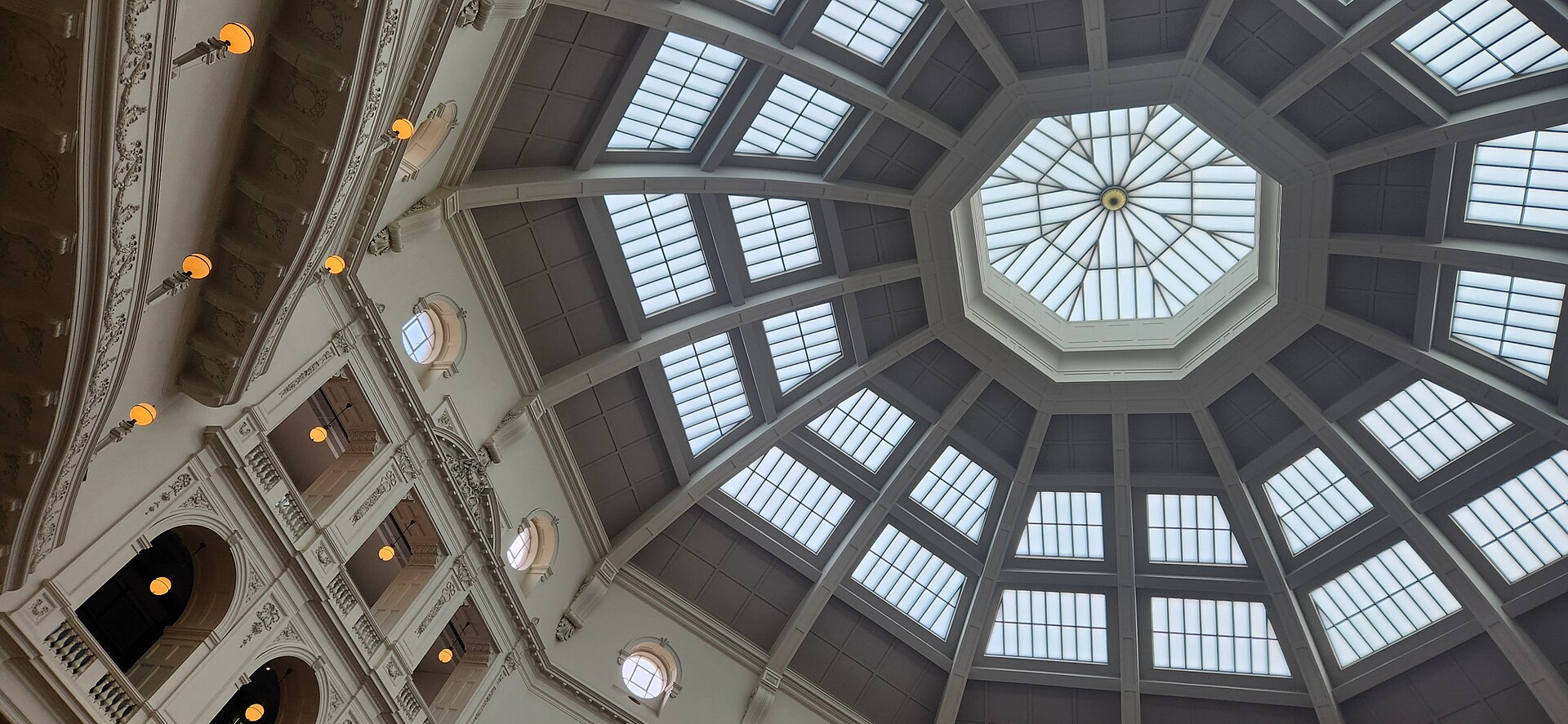 An ornate interior of the State Library Victoria features a large octagonal dome with skylights and balconies.